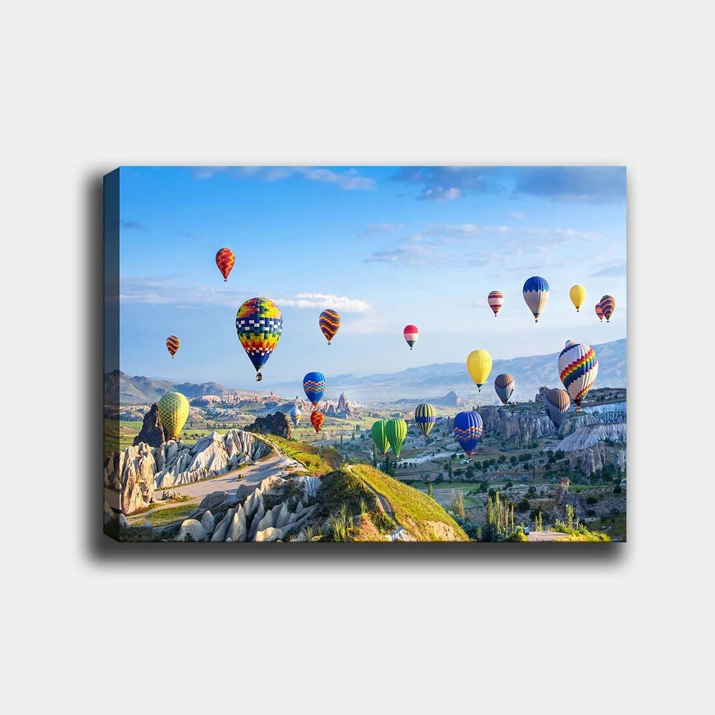 Canvastavla 70x100 cm - Färgglada varmluftsballonger sväva över en vacker landskapsscen i Cappadocia - Grön / Blå / Gul
